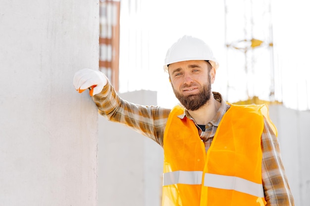 Builder repairman foreman in safety helmet and vest works at his workplace in a building under construction