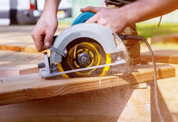 Photo builder saws a board with a circular saw in the cutting a wooden plank