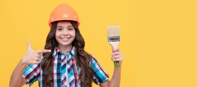 Builder teenager girl in helmet happy child with curly hair in construction helmet pointing finger