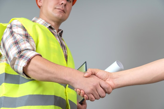 Foto un costruttore in abiti da lavoro, stringe la mano a un cliente su uno sfondo grigio.