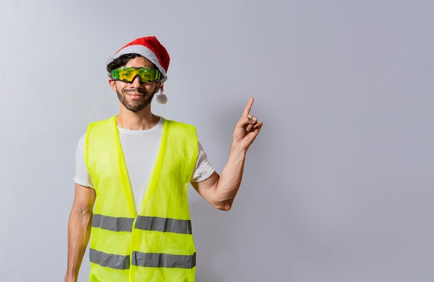 승진에 손가락을 가리키는 크리스마스 모자를 쓴 건축업자 오른쪽을 가리키는 크리스마스 모자를 쓴 건축업자 엔지니어 광고를 가리키는 크리스마스 모자를 쓴 건설 노동자