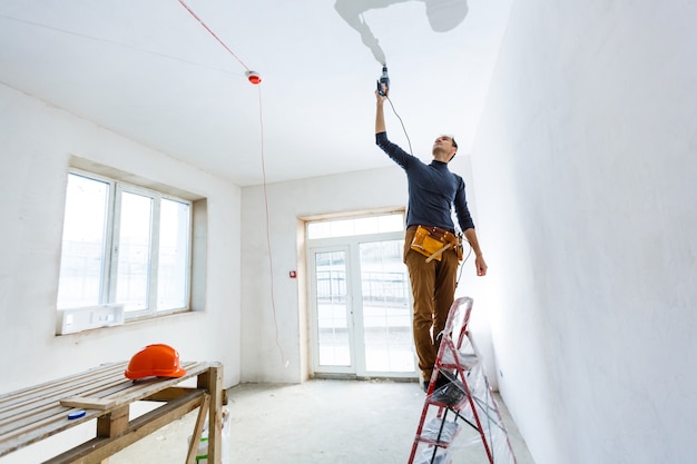 Builder worker with pneumatic hammer drill perforator equipment making hole in wall at construction site