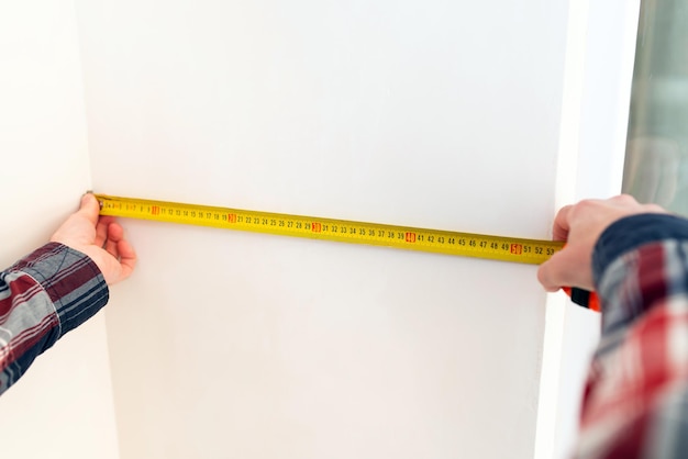 Builderrepairman measures the width of the wall with a tape measure