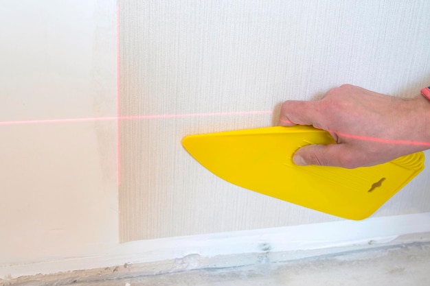 Builders hand smoothes the wallpaper with a plastic spatula on the wall during repair