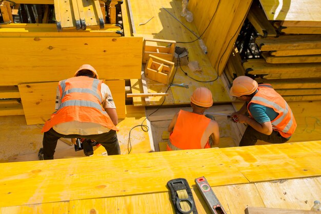 Builders installing formwork from wooden panels at a construction site