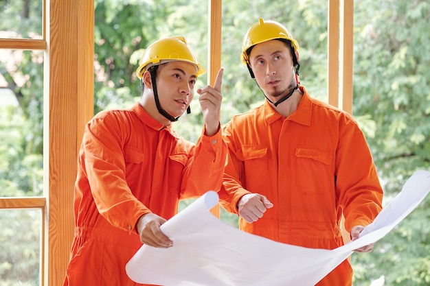 Builders with construction plan in hands discussing house walls they need to rebuild