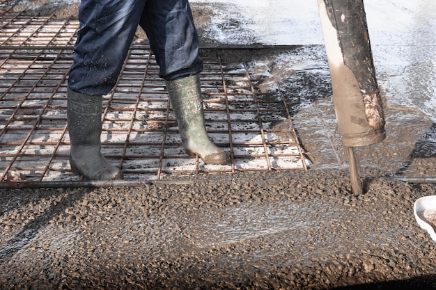 Builders workers pour concrete floor in industrial workshop Legs in boots in concrete Submission of concrete for pouring the floor Monolithic concrete works