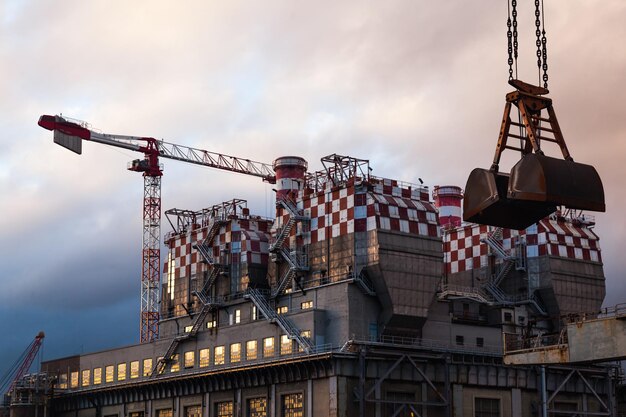 The building of a coal plant with cranes and an exhaust pipe at dusk