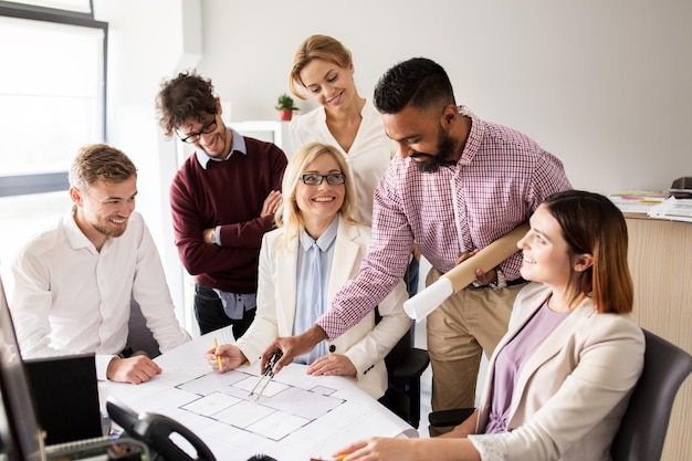 building, construction, architecture, real estate and people concept - business team with blueprint and dividers meeting and discussing house project at office