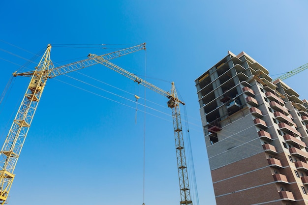 Building under construction and cranes on a blue sky background