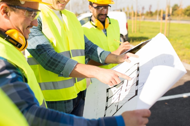 building, construction, development, teamwork and people concept - close up of builders high visible vests with blueprint at building site