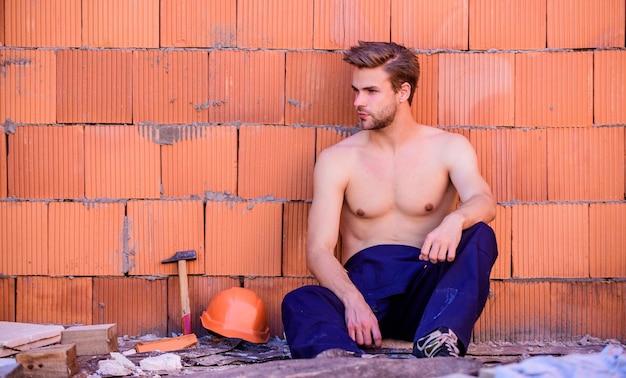 Building construction. General maintenance repair worker fix maintain building. Worker brick wall background. Man build own house. Attractive worker. Handsome sexy laborer. Inspecting building.