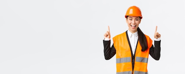 Building construction and industrial concept Happy smiling female asian engineer in safety helmet and reflective clothing introduce new object estate for sale Architect pointing fingers up