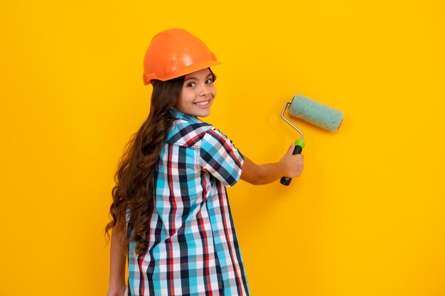 Building construction and profession girl in protective helmet with paint roller over yellow background