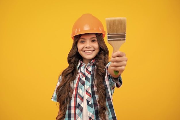 Building construction and profession girl in protective helmet with paint roller over yellow background