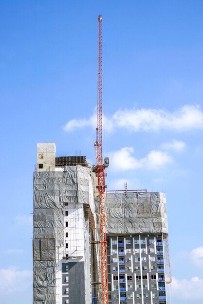 Building under construction with hoisting cranes on bright blue sky background