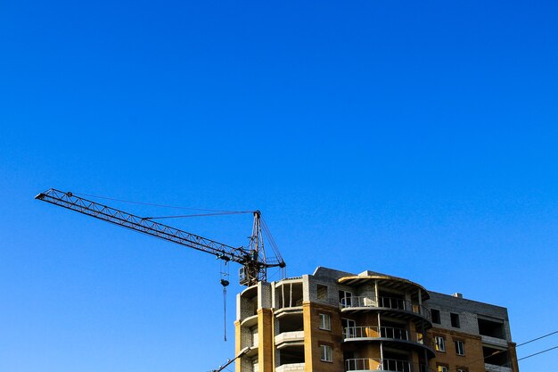 Building crane and building under construction against blue sky