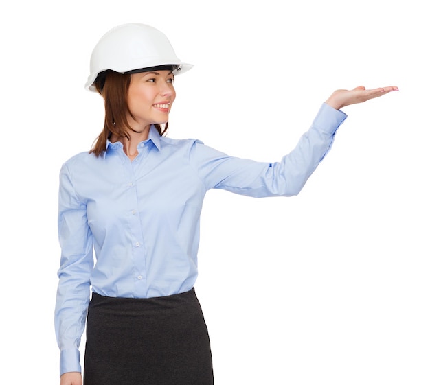 building, developing, advertising and architecture concept - friendly young smiling businesswoman in white helmet holding something on palm