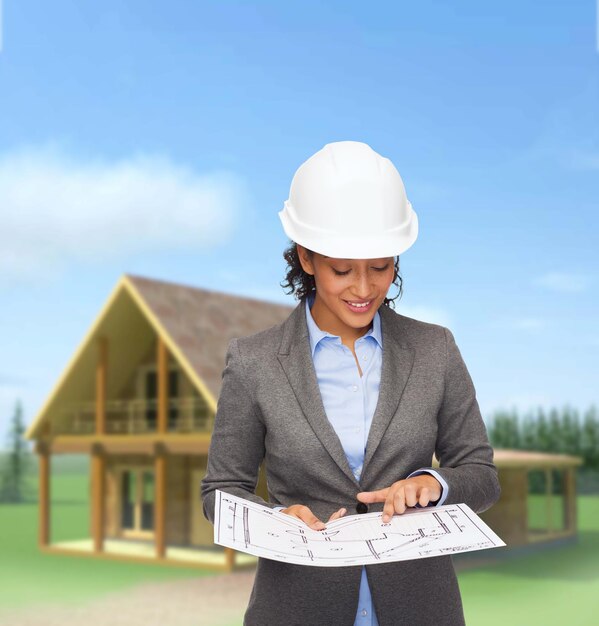 building, developing, consrtuction and architecture concept - smiling businesswoman in white helmet pointing finger to blueprint