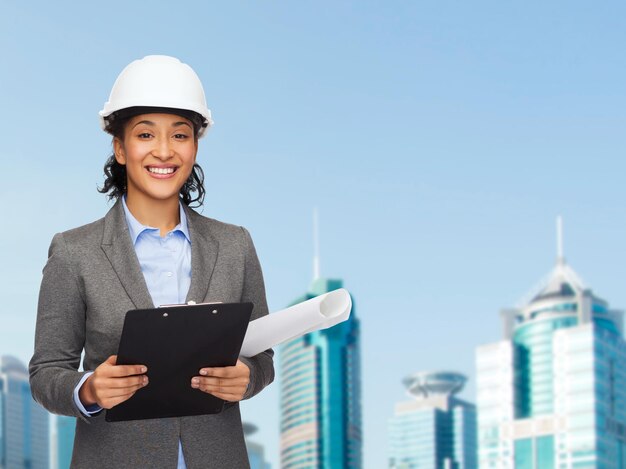 building, developing, consrtuction and architecture concept - smiling businesswoman in white helmet with clipboard and blueprint