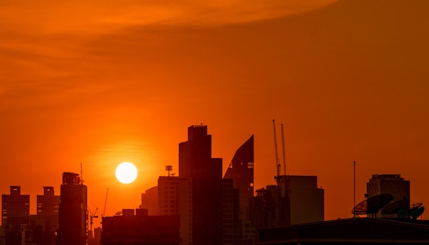 美しい夕焼け空と夕暮れ時にダウンタウンの建物。夜のマンションとアパートのシルエット。高層ビルの建物と建設クレーンの街並み。