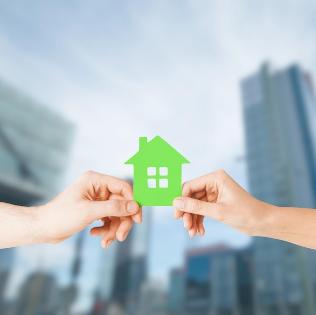 building, family and real estate concept - closeup picture of woman and man hands holding green house