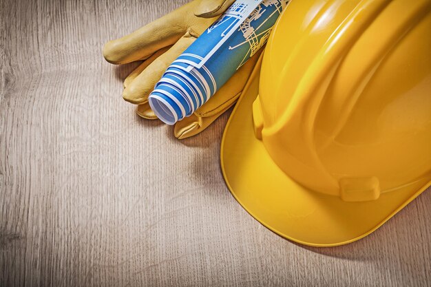 Building helmet leather protective gloves blue blueprints on wooden board construction concept