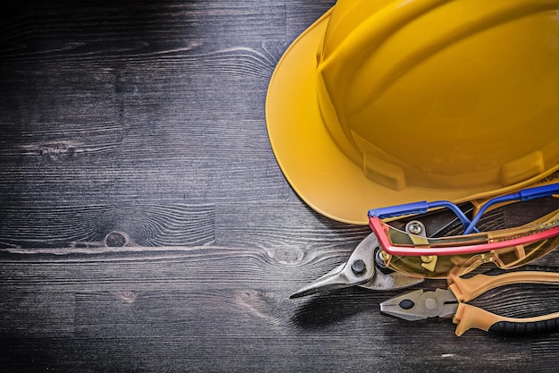 Building helmet safety glasses pliers tin snips on wooden background