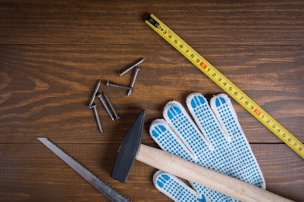 Building implements. Hammer, nails, hacksaw, measuring tape measure and gloves on a wooden.