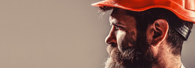 Building, industry, technology - builder concept. Bearded man worker with beard in building helmet or hard hat. Man builders, industry. Builder in hard hat, foreman or repairman in the helmet