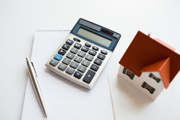 building, mortgage, real estate and property concept - close up of home model, house keys and notebook with pen