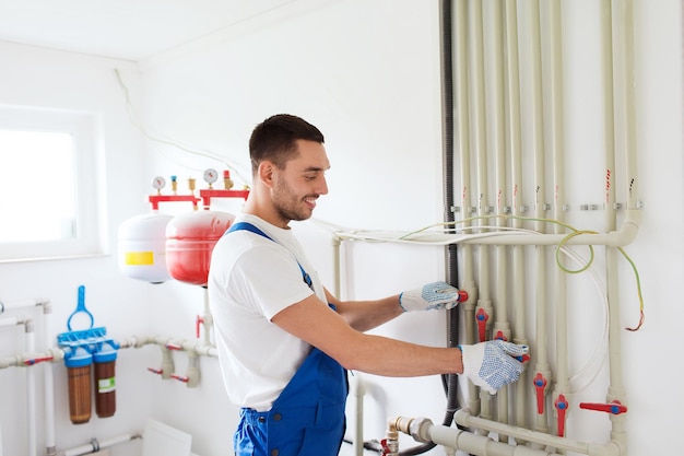 building, profession and people concept - builder or plumber working with water pipes in boiler room