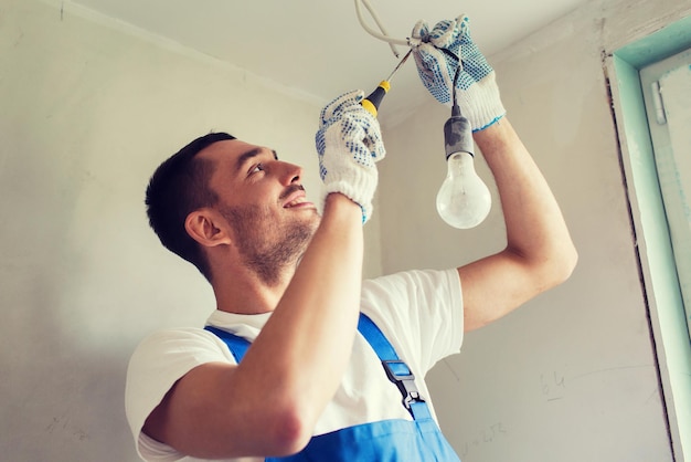 building, renovation, technology, electricity and people concept - builder with screwdriver fixing socket indoors