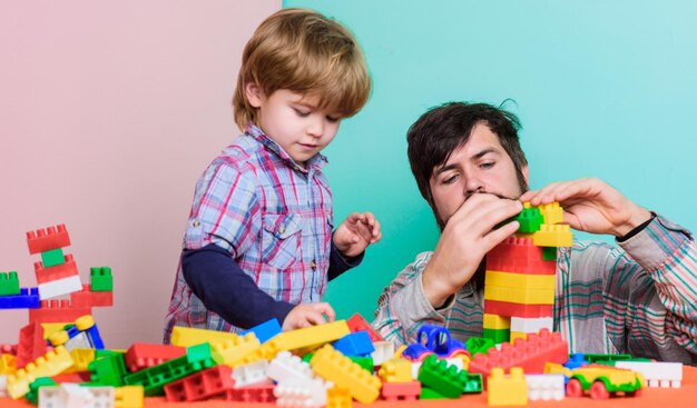 カラフルなコンストラクターを持つ建物は、子供の発達が大好きです父と息子が一緒に遊んでいるお父さんと一緒にゲームをする小さな男の子幸せな家族の余暇の助けとサポートは私にあなたの家族のサポートを手伝わせます