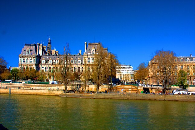 Buildings by river against clear blue sky