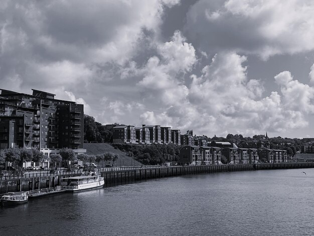 Photo buildings by river against cloudy sky