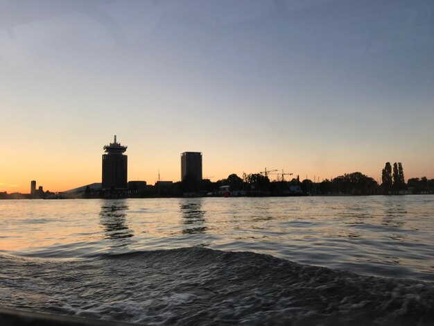 Buildings by sea against clear sky during sunset