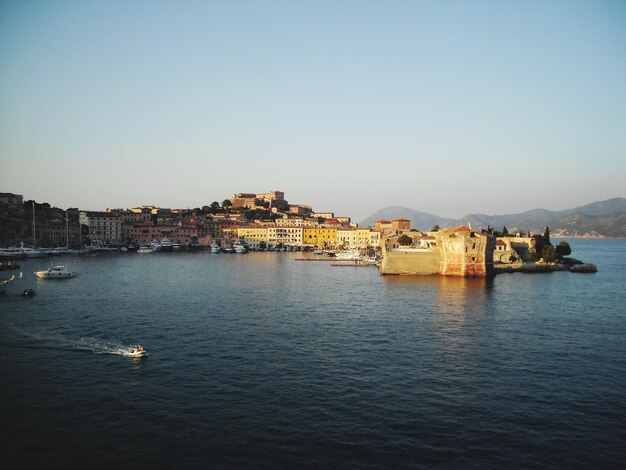 Buildings by sea against clear sky