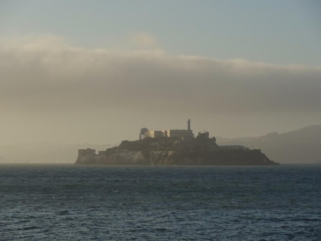 Buildings by sea against cloudy sky