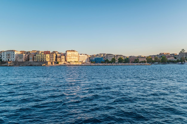 Edifici dell'isola di corfù sulla riva e sull'acqua di mare al tramonto