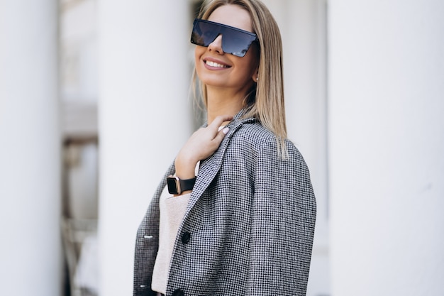 Buiten foto van blonde dame poseren op het platform achtergrond in herfstdag. Mode Streetstyle portret. een donkere vrijetijdsbroek en een romige trui en een zonnebril dragen. Mode concept.