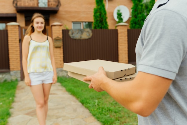 Buiten gaat de foto van de lieve schattige vrouw naar de bezorger om een pizza te halen, vlakbij het woonhuis.