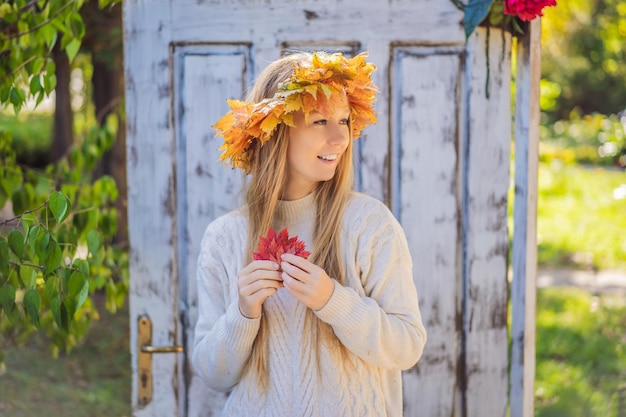 Buiten levensstijl close-up portret van charmante blonde jonge vrouw die een krans van herfstbladeren draagt