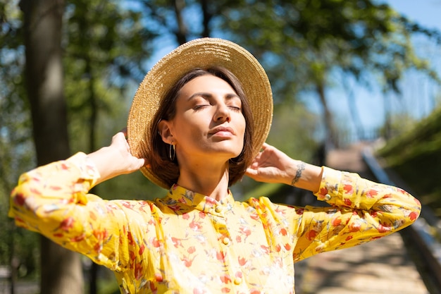 Buiten mode nauwe portret van vrouw in gele zomerjurk en hoed in het park, genieten van warme zomerdagen
