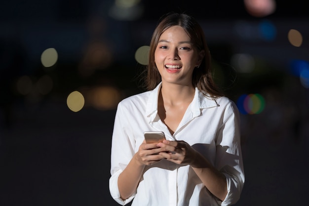 Buiten portret van jonge vrouw met smileygezicht met behulp van een telefoon loopt in een stad