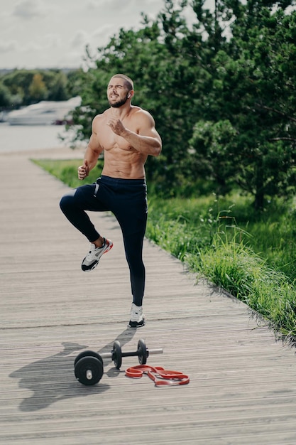 Buiten schot van knappe fit gespierde bebaarde man doet hoge knie-tap oefening warmt op voordat hardlopen cardiotraining heeft gebruikt sportuitrusting heeft sterk lichaam toont vastberadenheid