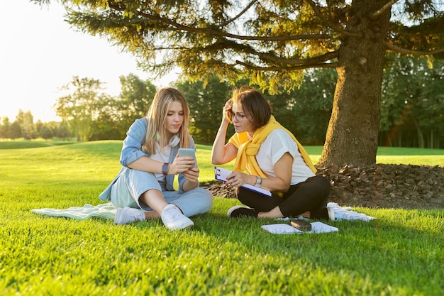 Buiten vergadering van tienermeisje en vrouw van psycholoog maatschappelijk werker, vrouwen praten zittend op groen gazon in park, comfortabele omgeving om te praten met jongeren, geestelijke hulp overleg