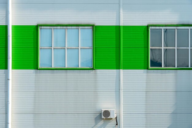 Buitenairconditionereenheid aan de muur van een fabriek of fabriek De buitenmuur van de onderneming is gemaakt van witte en groene metalen profielen met afvoerbuizen en grote ramen met ruimte voor tekstkopie