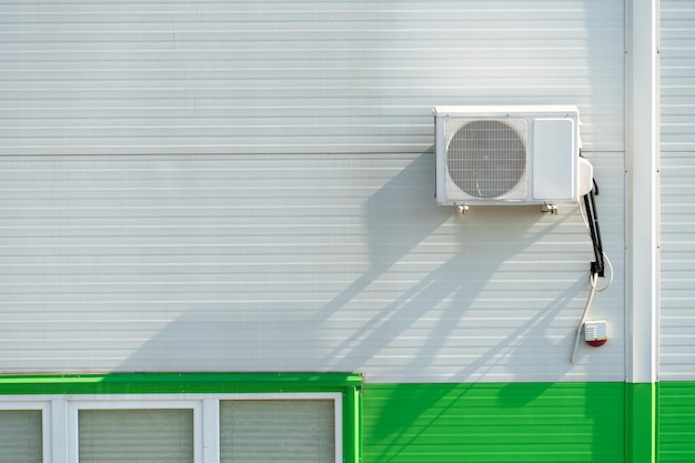 Buitenairconditionereenheid aan de muur van een fabriek of fabriek De buitenmuur van de onderneming is gemaakt van witte en groene metalen profielen met afvoerbuizen en grote ramen met ruimte voor tekstkopie