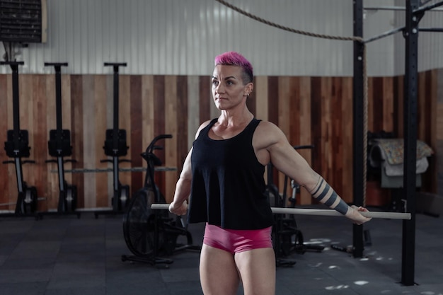 Buitengewone gespierde krachtige vrouw met roze haar oefent warming-up voor intensieve training in een moderne cross-gym.